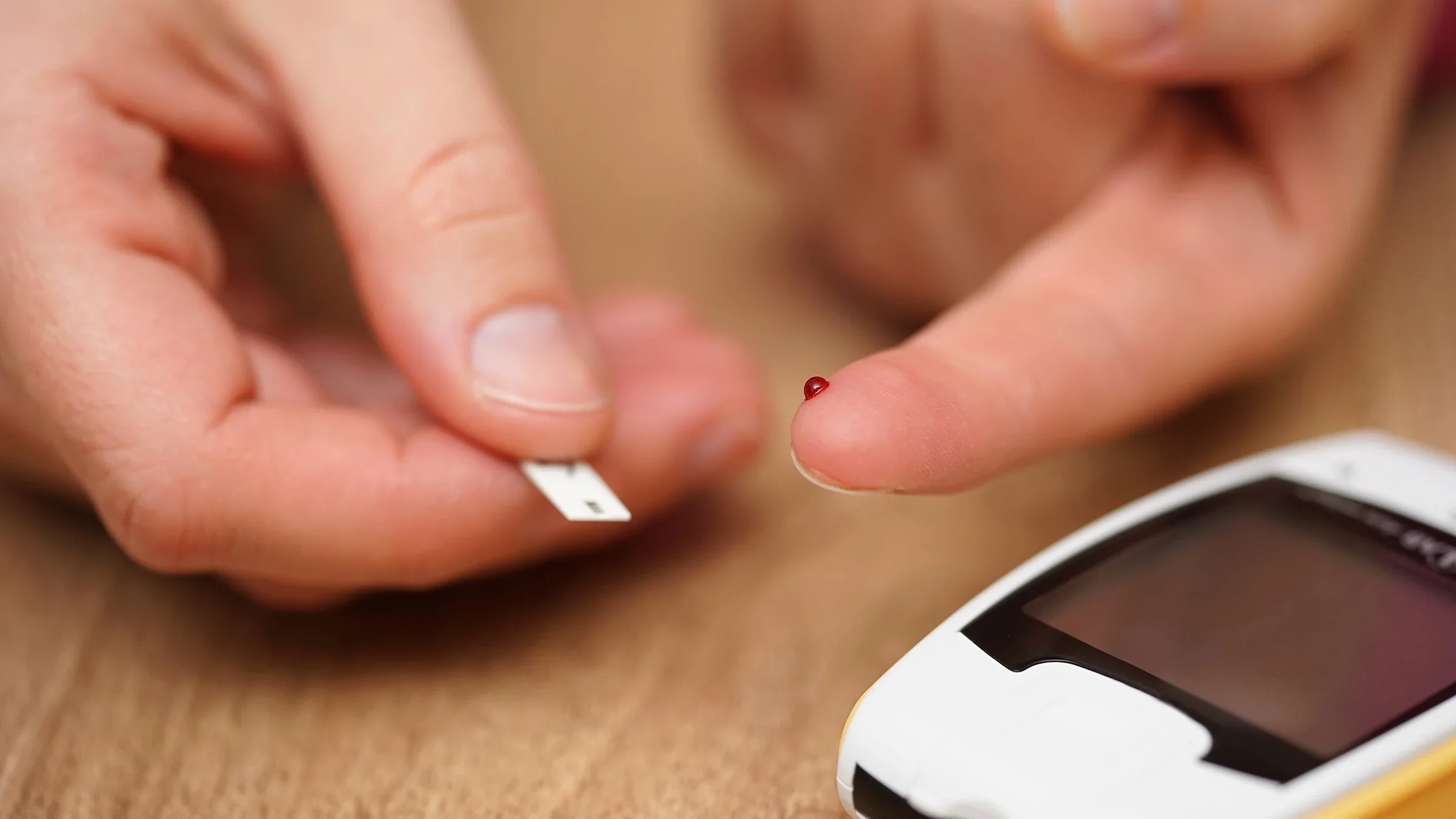 Persona en primer plano que usa glucómetro y tiras de prueba. Hay una pequeña gota de sangre en la punta de su dedo.
BernardaSv/iStock vía Getty Images