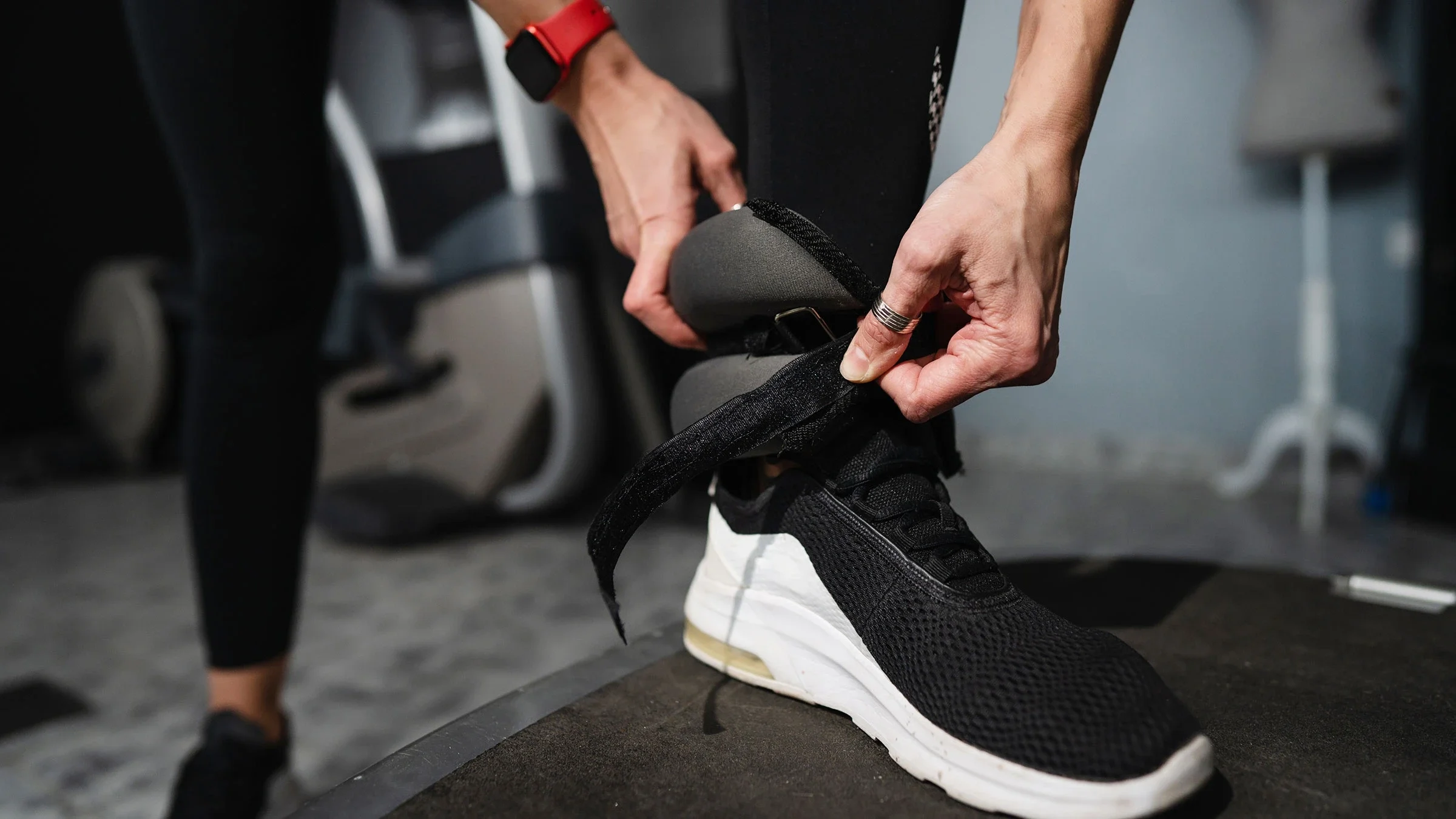 A woman puts on an ankle weight at the gym.