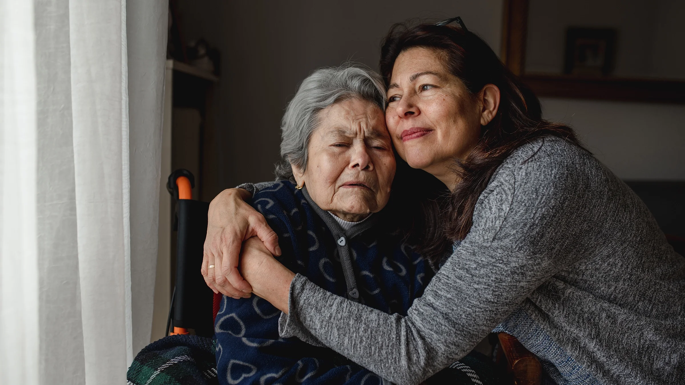 A woman hugs her mother, who’s sitting in a wheelchair.
