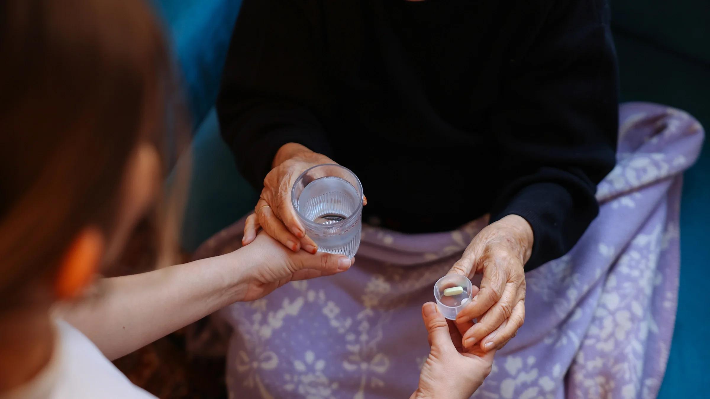 A caregiver hands a dose of medication and a glass of water to their loved one.
