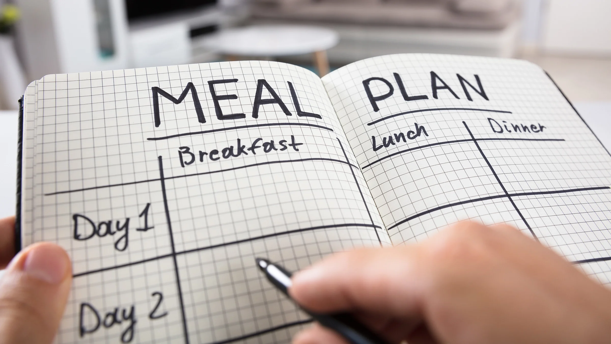 A person fills out a meal plan in a checkered notebook.