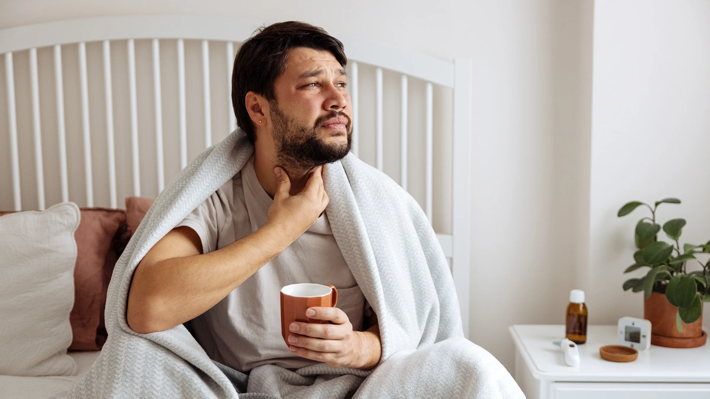 A man with the flu touches his sore throat.