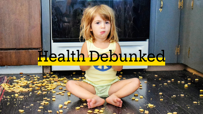 Toddler eating cereal off the floor. There is added text on top reading “Health Debunked” with a yellow highlight bar behind it.