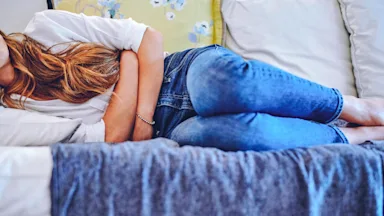 A cropped shot of a person in pain on their couch.
Charday Penn/E+ via Getty Images