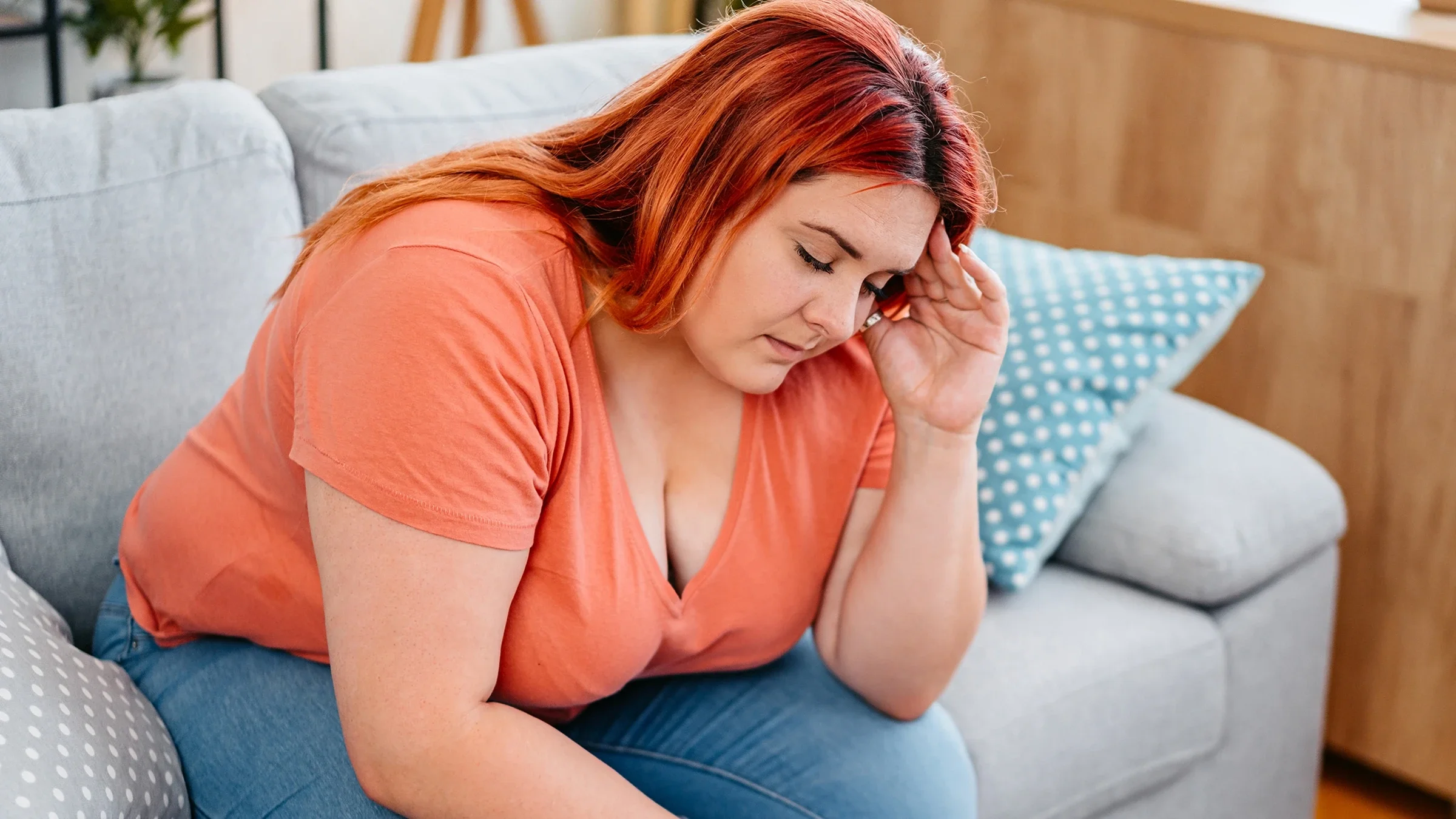 A woman touches her temple as she experiences a headache while sitting on a sofa.