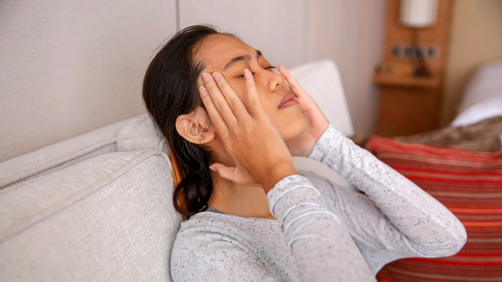 A woman sitting on the sofa looking stressed and worried.