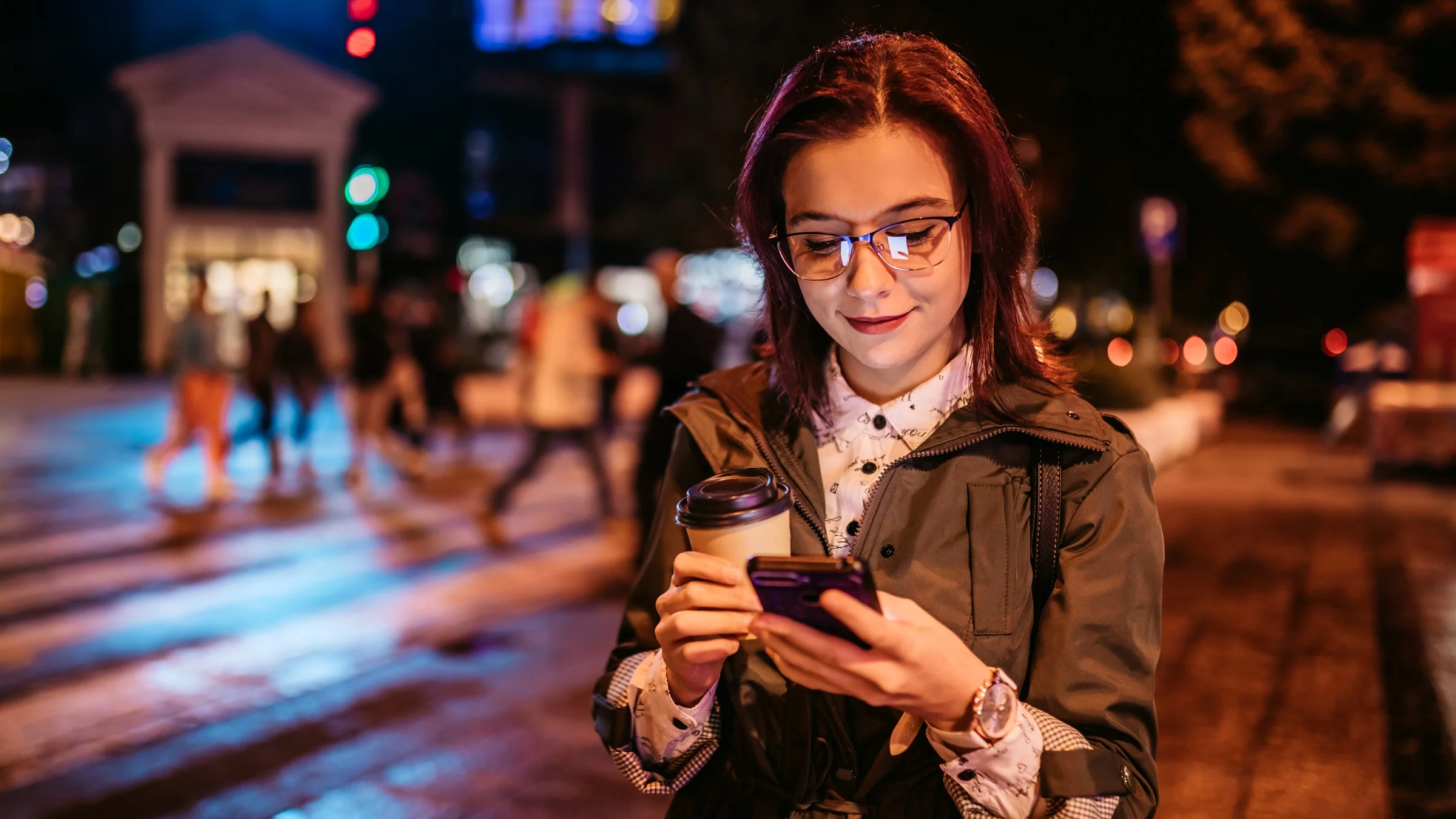A person holding a coffee and using their phone at night.