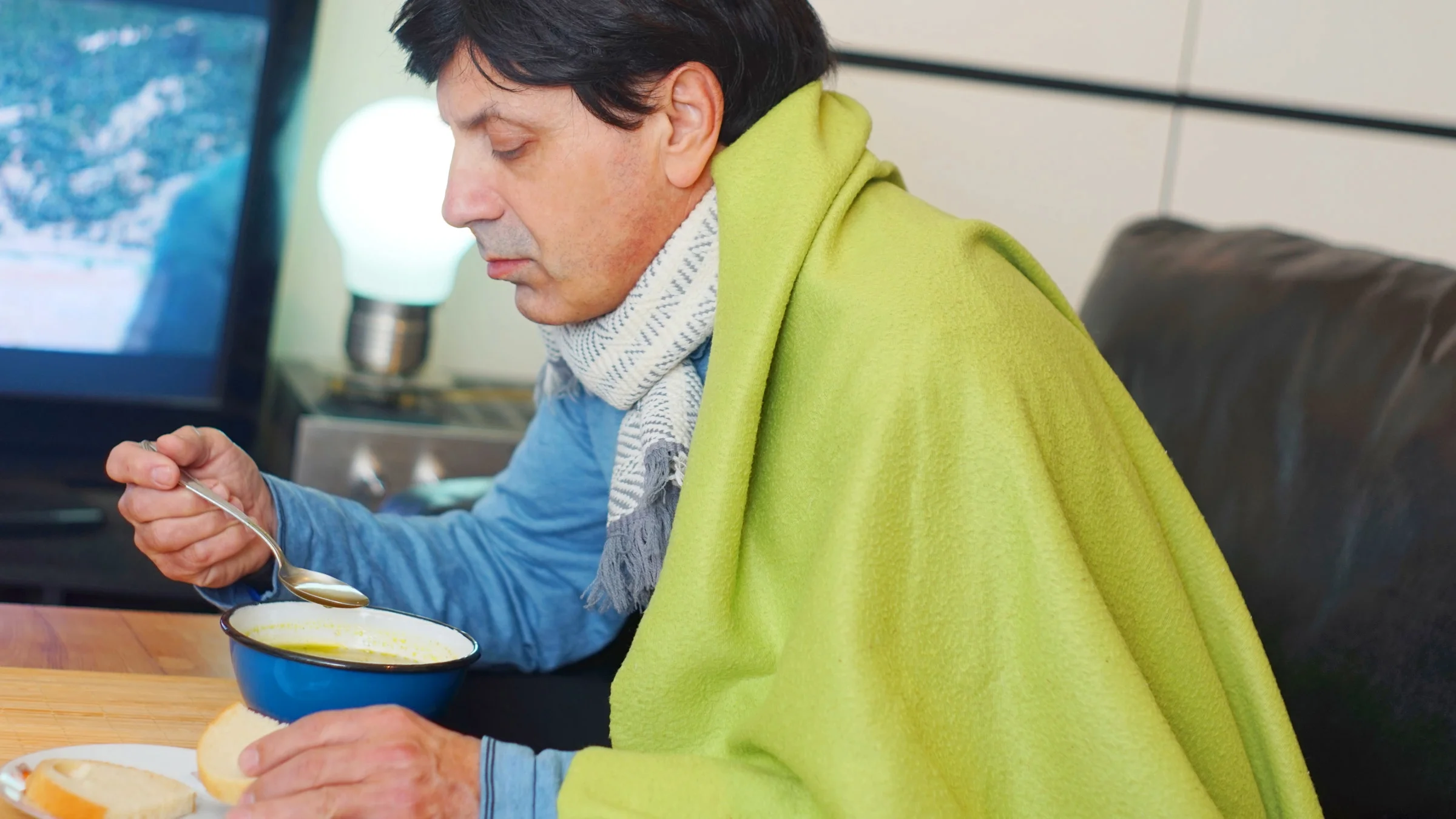 A sick person drinking soup and eating bread.