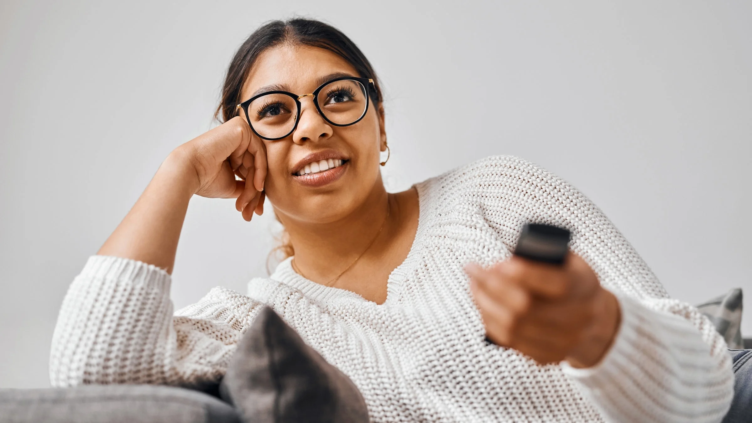 A person sitting on their couch watching TV, holding a remote control.