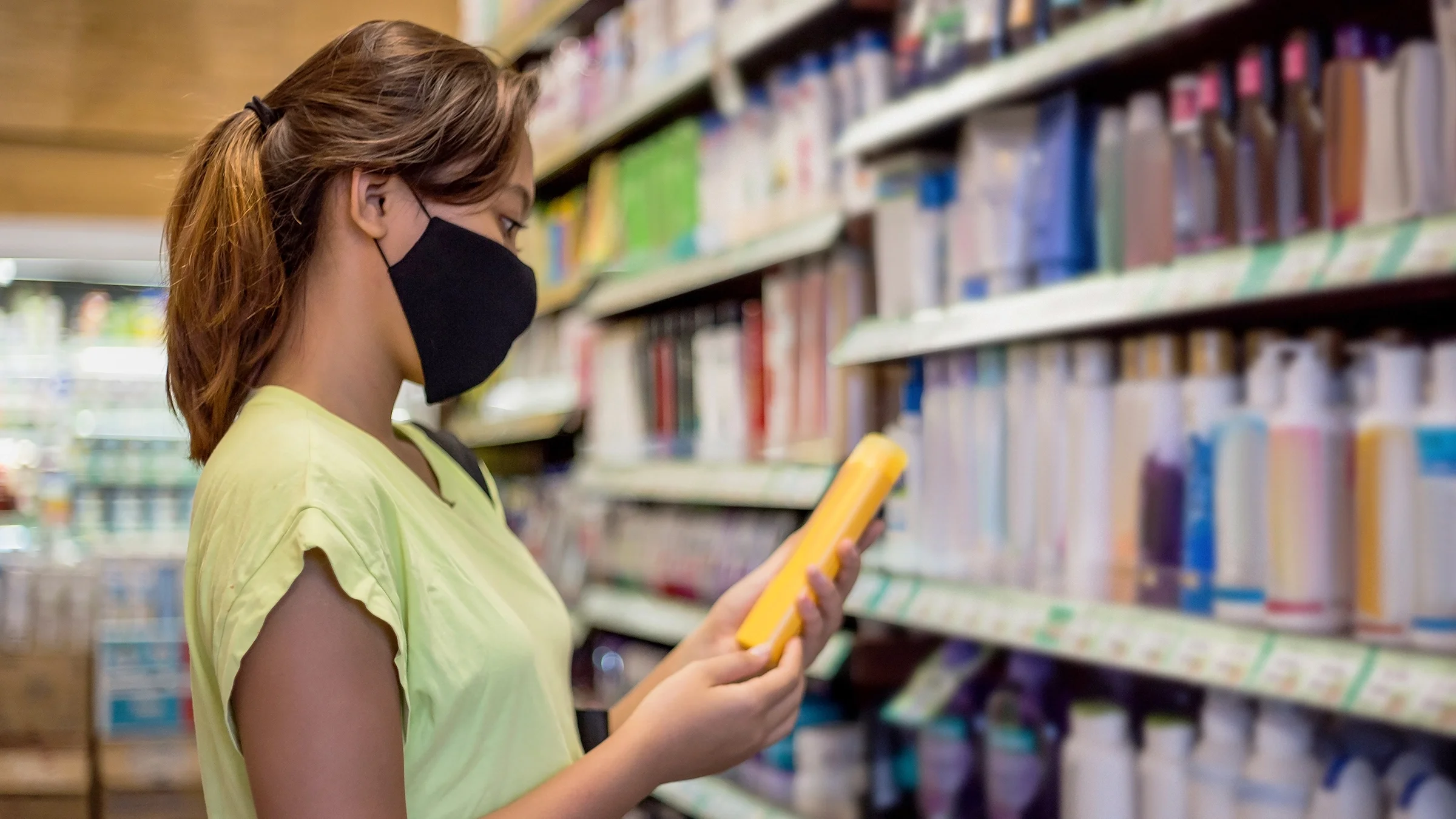 A woman reads the label on the back of a shampoo bottle.
