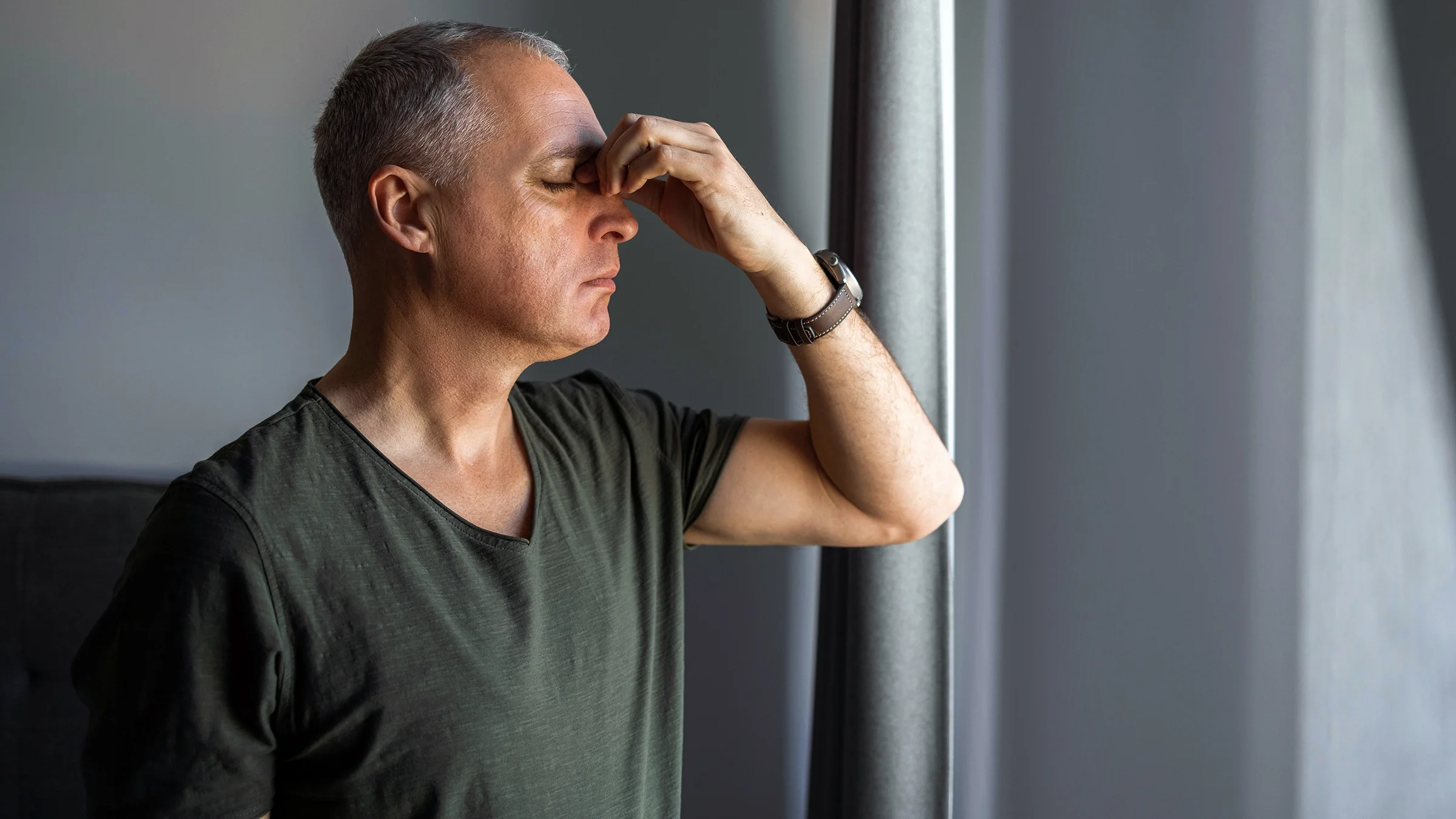 A man pinches the bridge of his nose as he deals with sinus pain.
