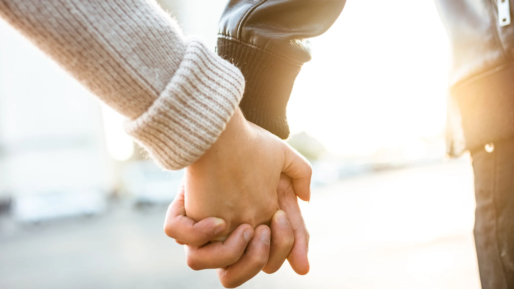 Close-up of two people holding hands with a sun flare in the background.