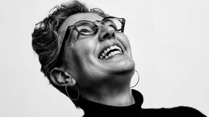 Black and white close-up portrait of an older woman with round glasses. She has her head tilted up to the sky smiling and you can see her neck exposed where her thyroid is.