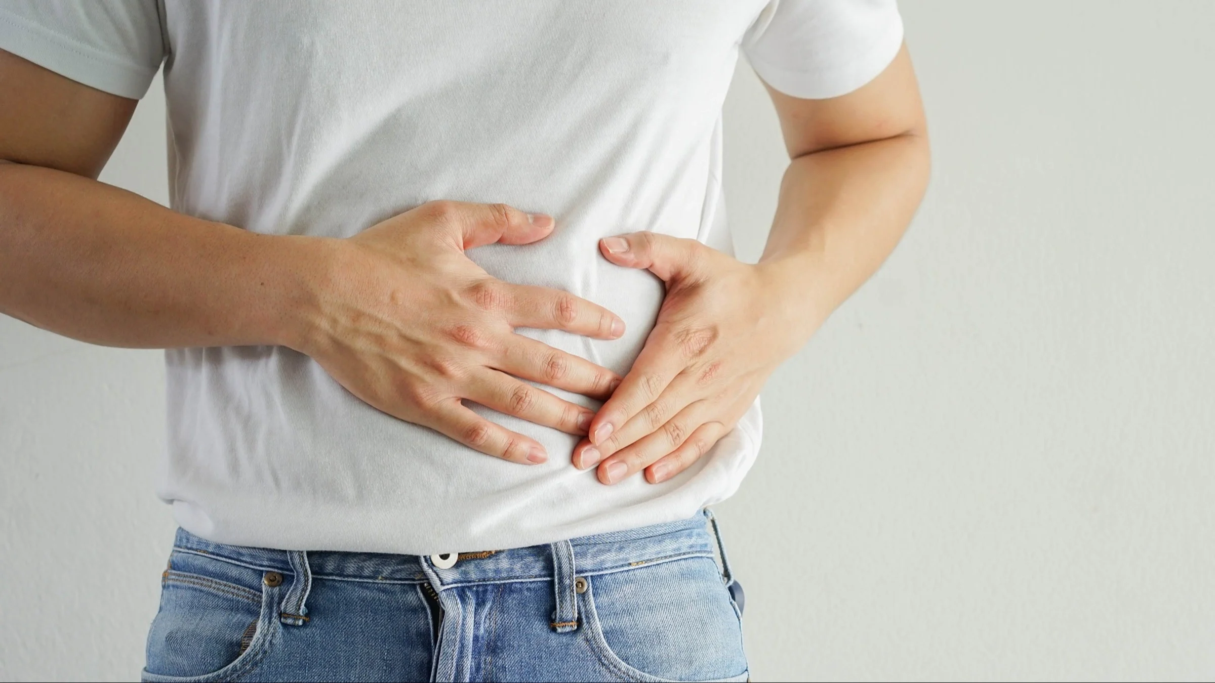 A close-up image shows a man in a white T-shirt and jeans holding his side abdomen.