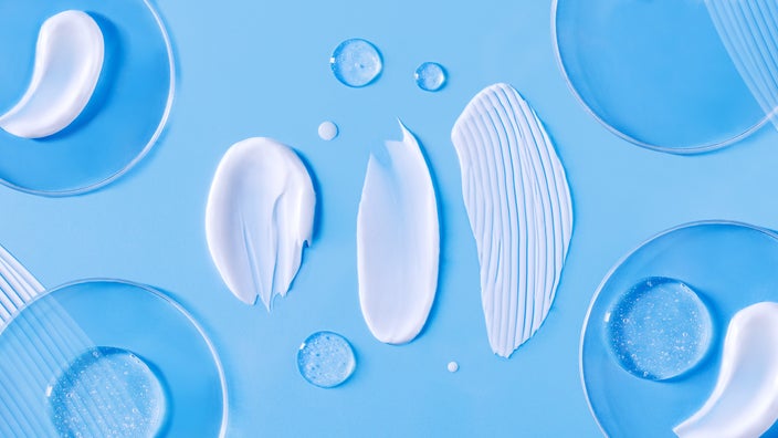 A close-up image shows smears of facial cream and serum on a blue surface.
