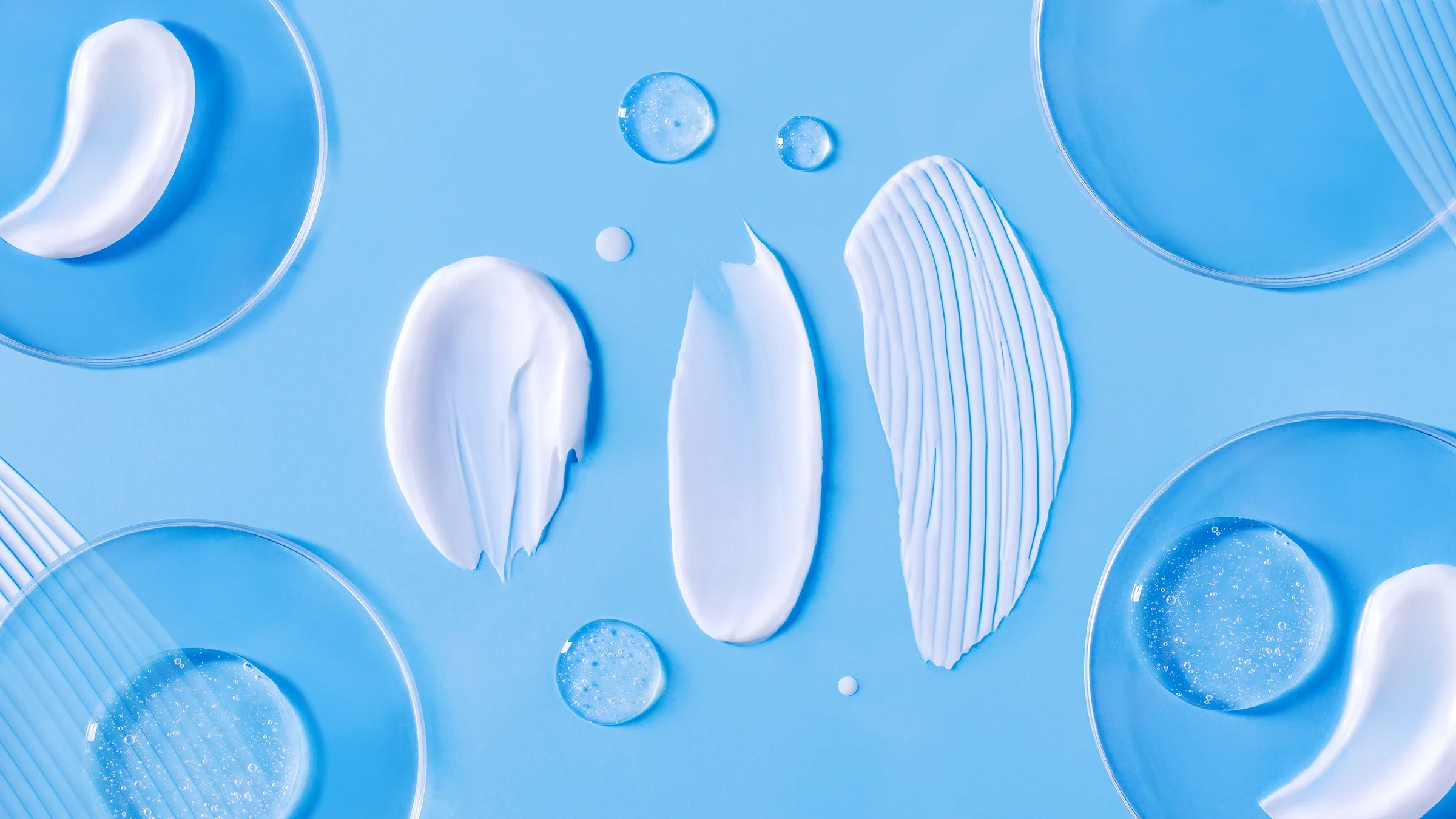 A close-up image shows smears of facial cream and serum on a blue surface.