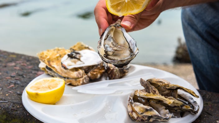 A person holding a lemon and oyster over a platter of raw oysters and lemon. 
