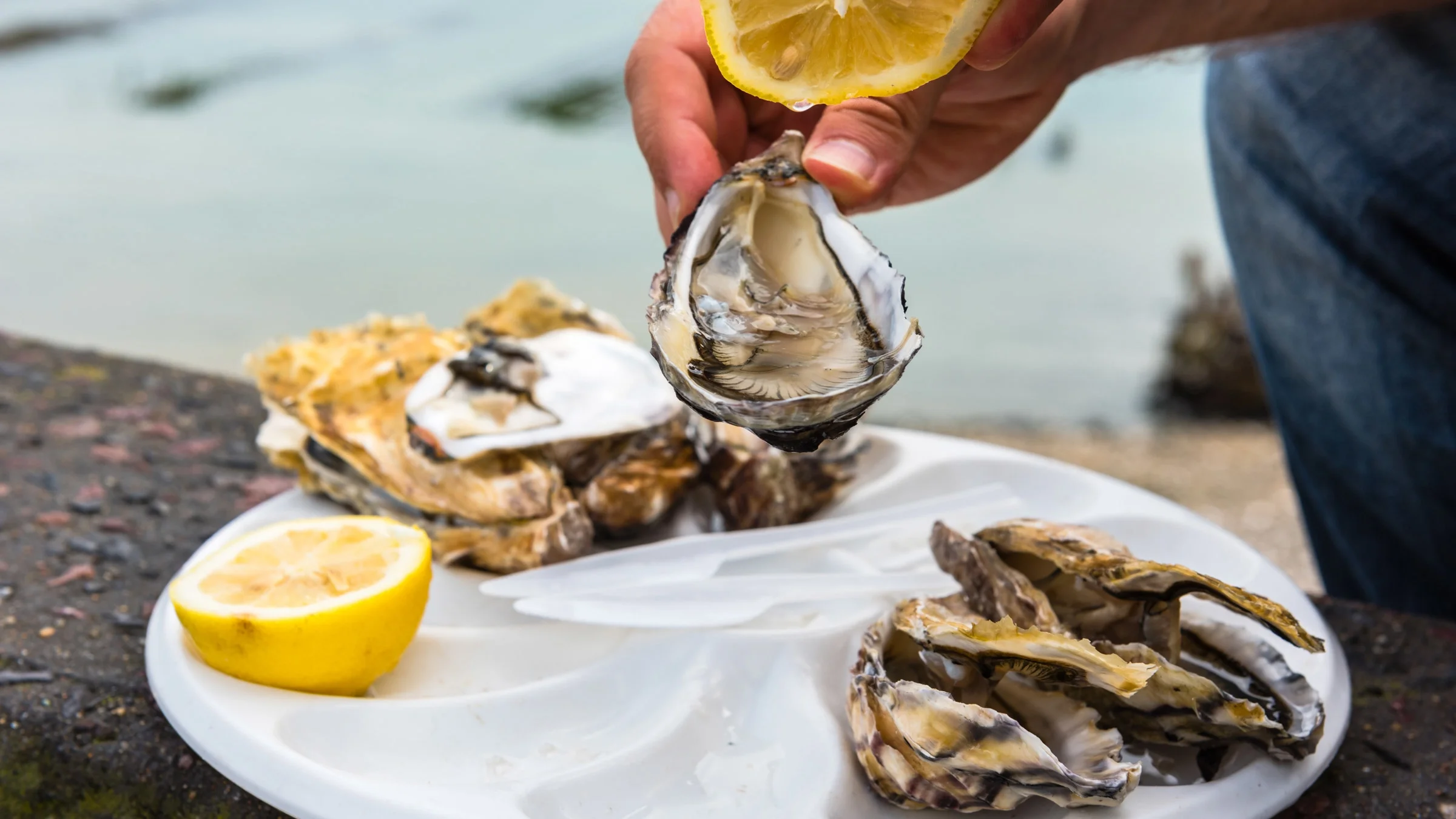 A person holding a lemon and oyster over a platter of raw oysters and lemon.