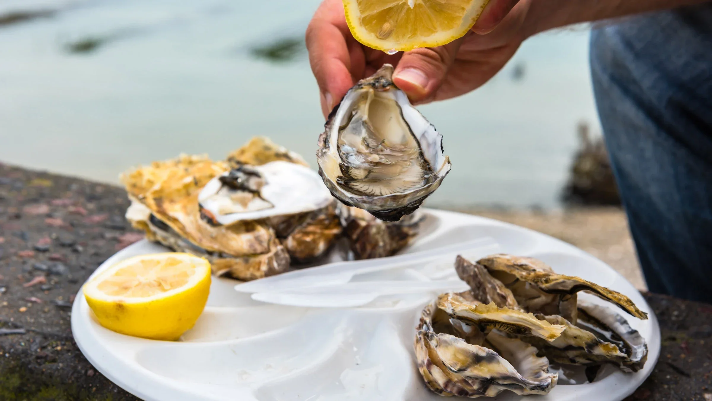A person holding a lemon and oyster over a platter of raw oysters and lemon. 
dvoevnore/iStock via Getty Images