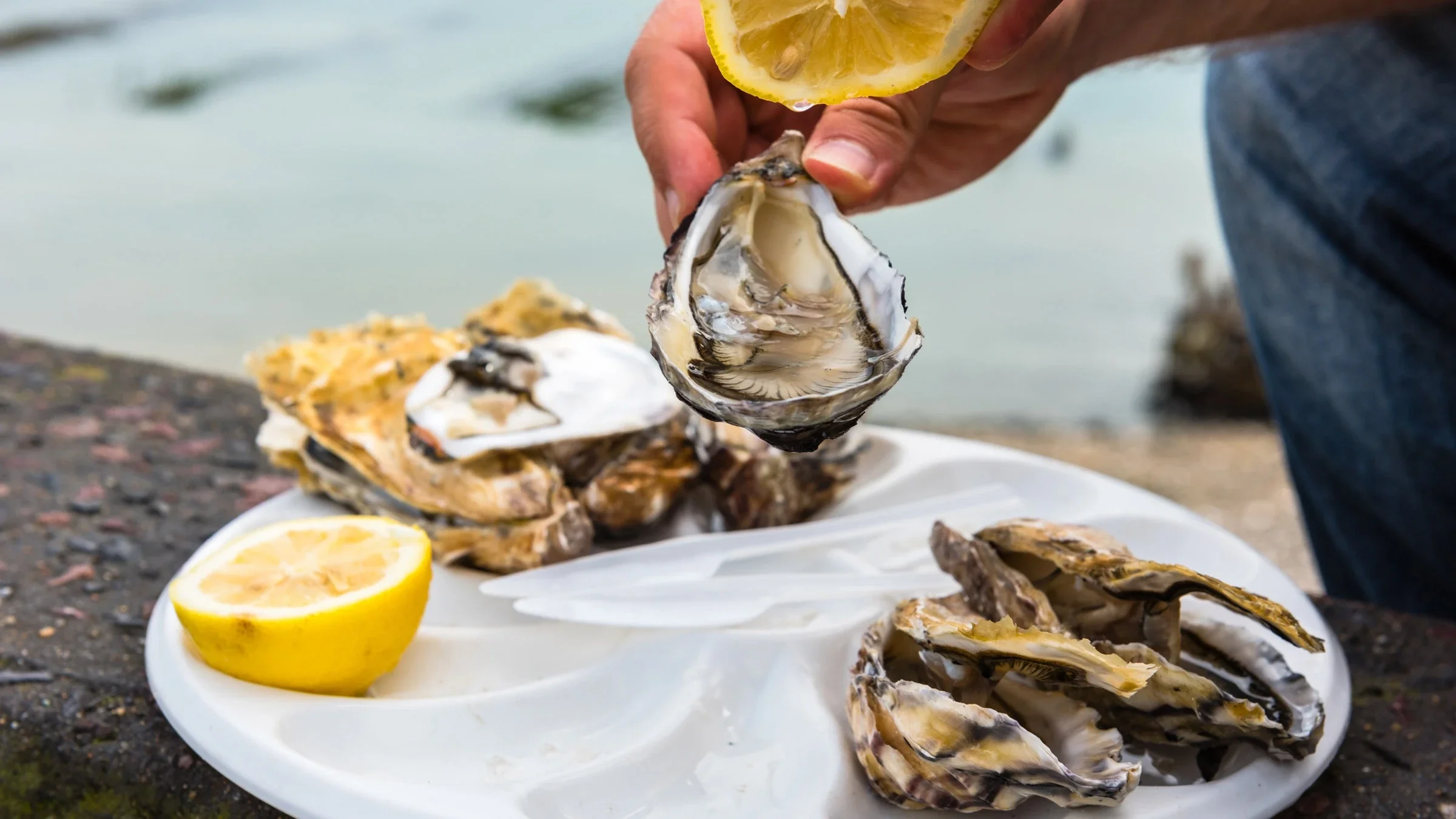 A person holding a lemon and oyster over a platter of raw oysters and lemon. 