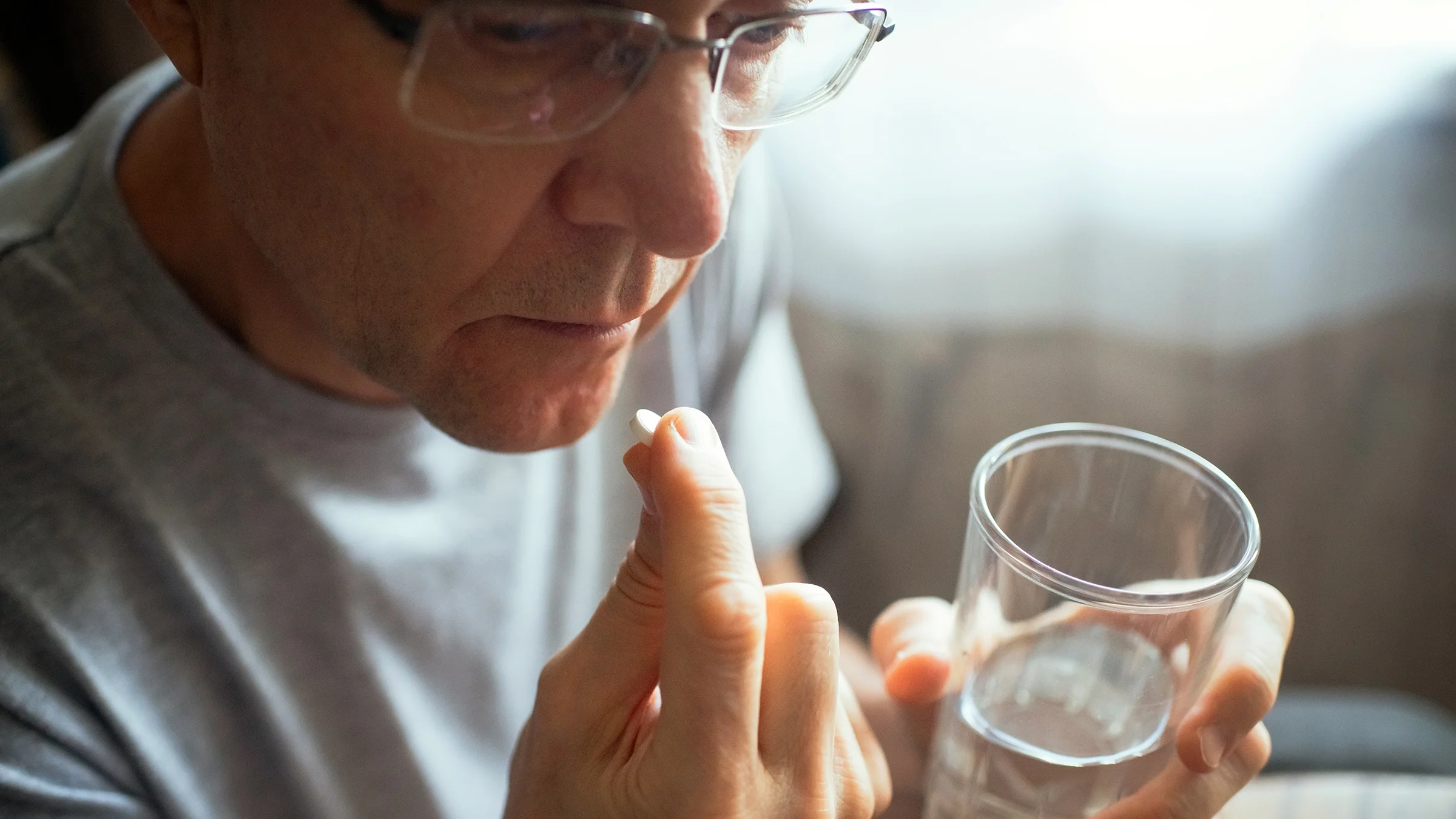 An older man takes a pill with a glass of water.