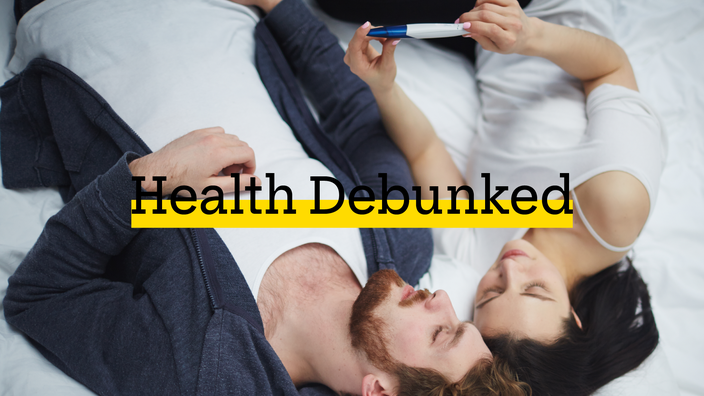 A couple in bed looking at a pregnancy test. There is added text on top reading “Health Debunked” with a yellow highlight bar behind it.