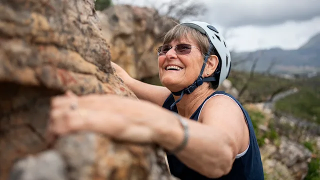 movement exercise: senior woman rock climbing outdoors 1942436826