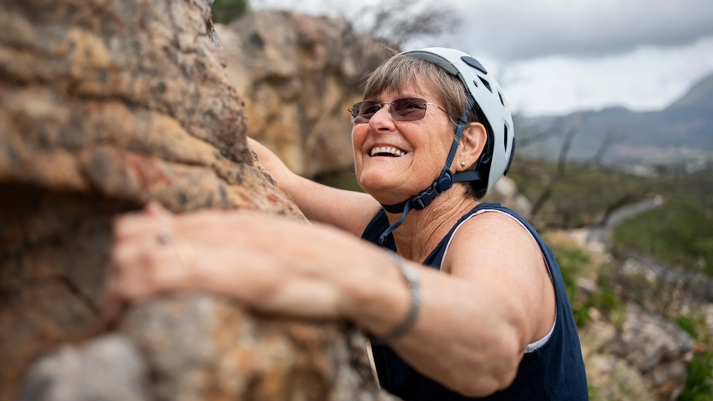 Smiling senior woman rock climbing outdoors.