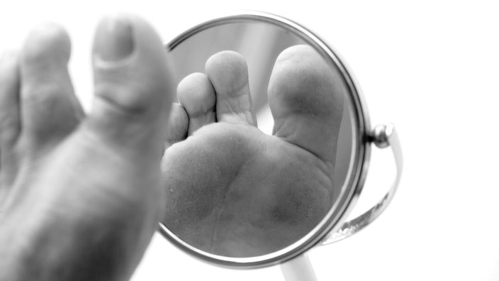 Black and white close-up on a person inspecting their foot in a hand held mirror.