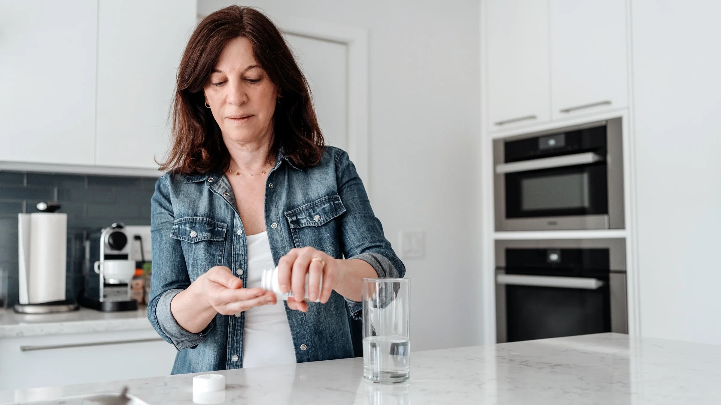 A woman is taking medication in her kitchen.