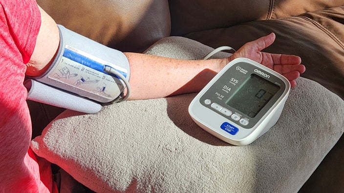 Mary Westheimer’s arm is shown, wearing a blood pressure cuff, resting on a pillow, and measuring her blood pressure.