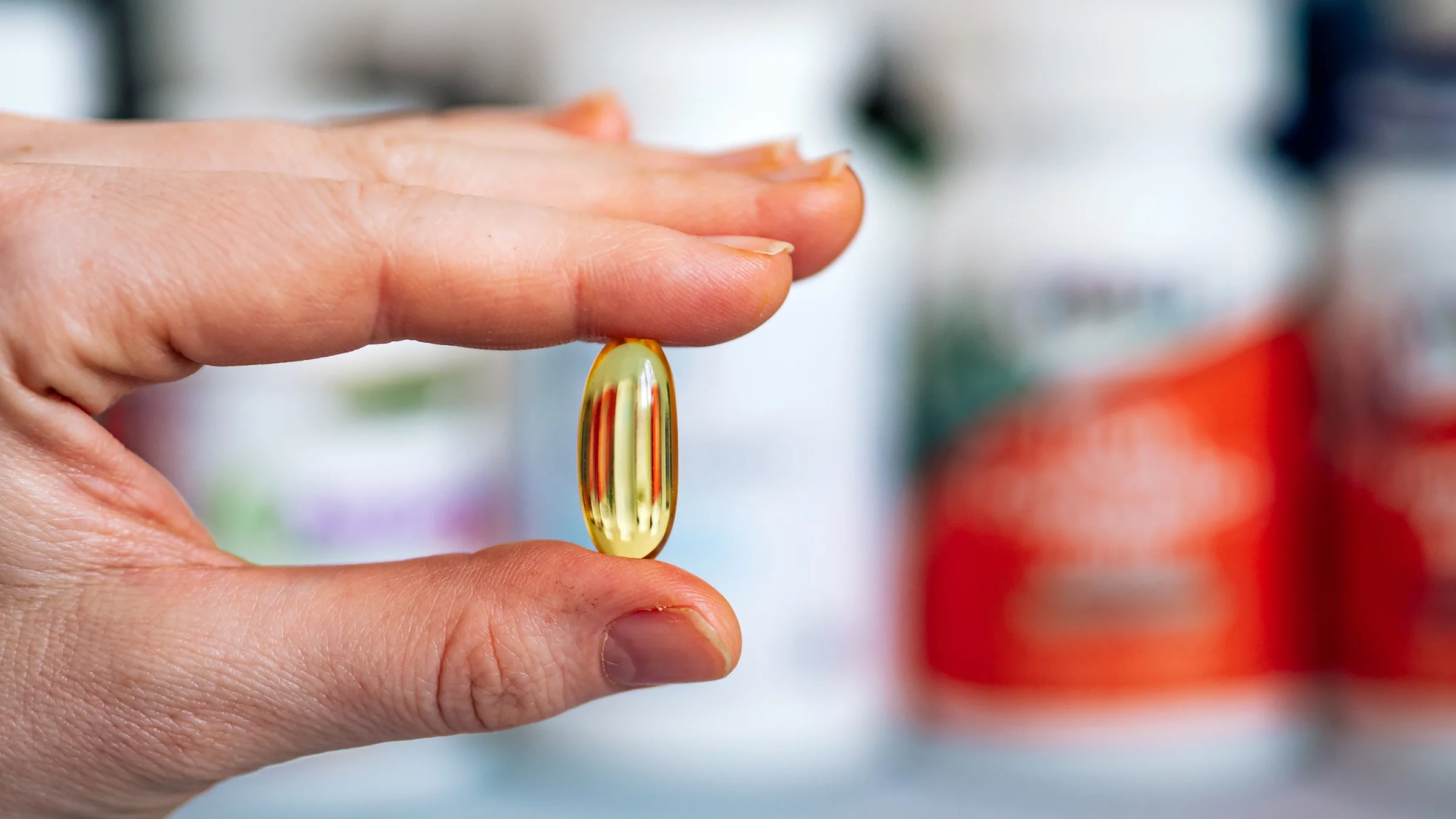 A person holds a yellow liquid gel pill in between their thumb and index finger.