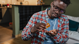 Man taking medicine from orange prescription bottle.
blackCAT/E+ via Getty Image