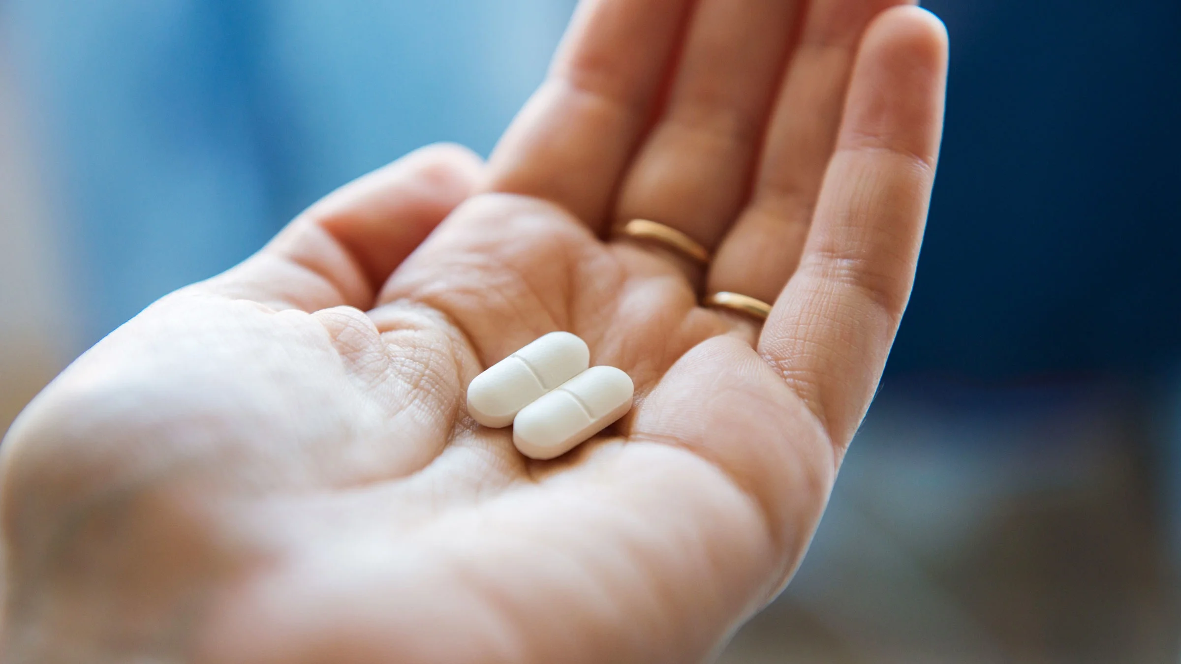 A close-up view of a hand holding two white pills in the palm.