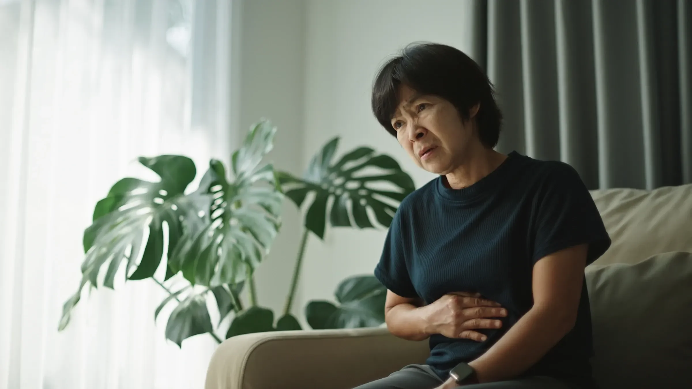 A person is sitting down and holding their belly like they have a stomachache.