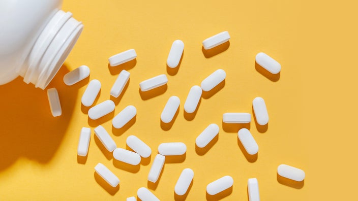 White pills poured from a jar on a yellow background