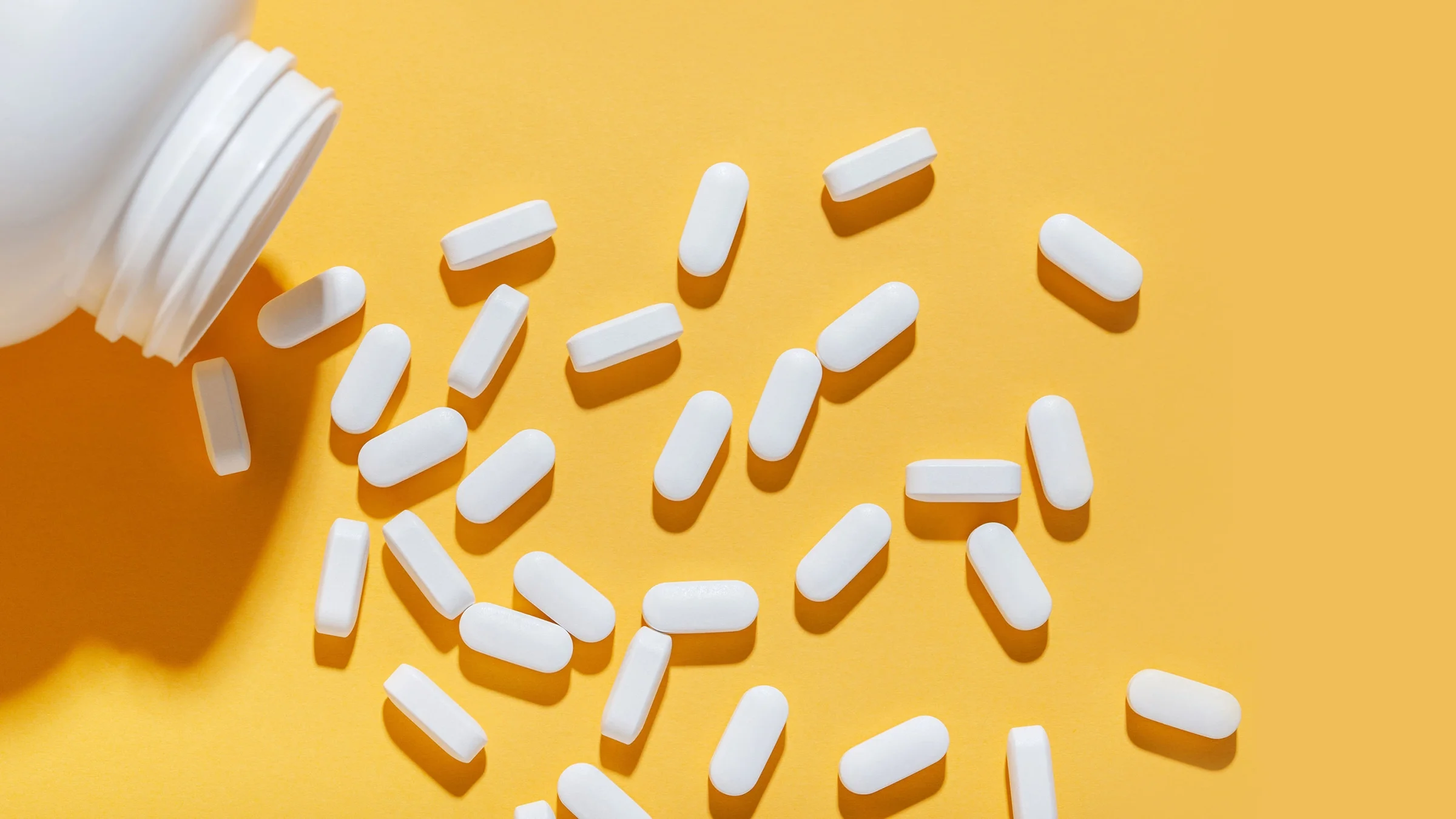 Pastillas blancas vertidas desde un frasco sobre un fondo amarillo