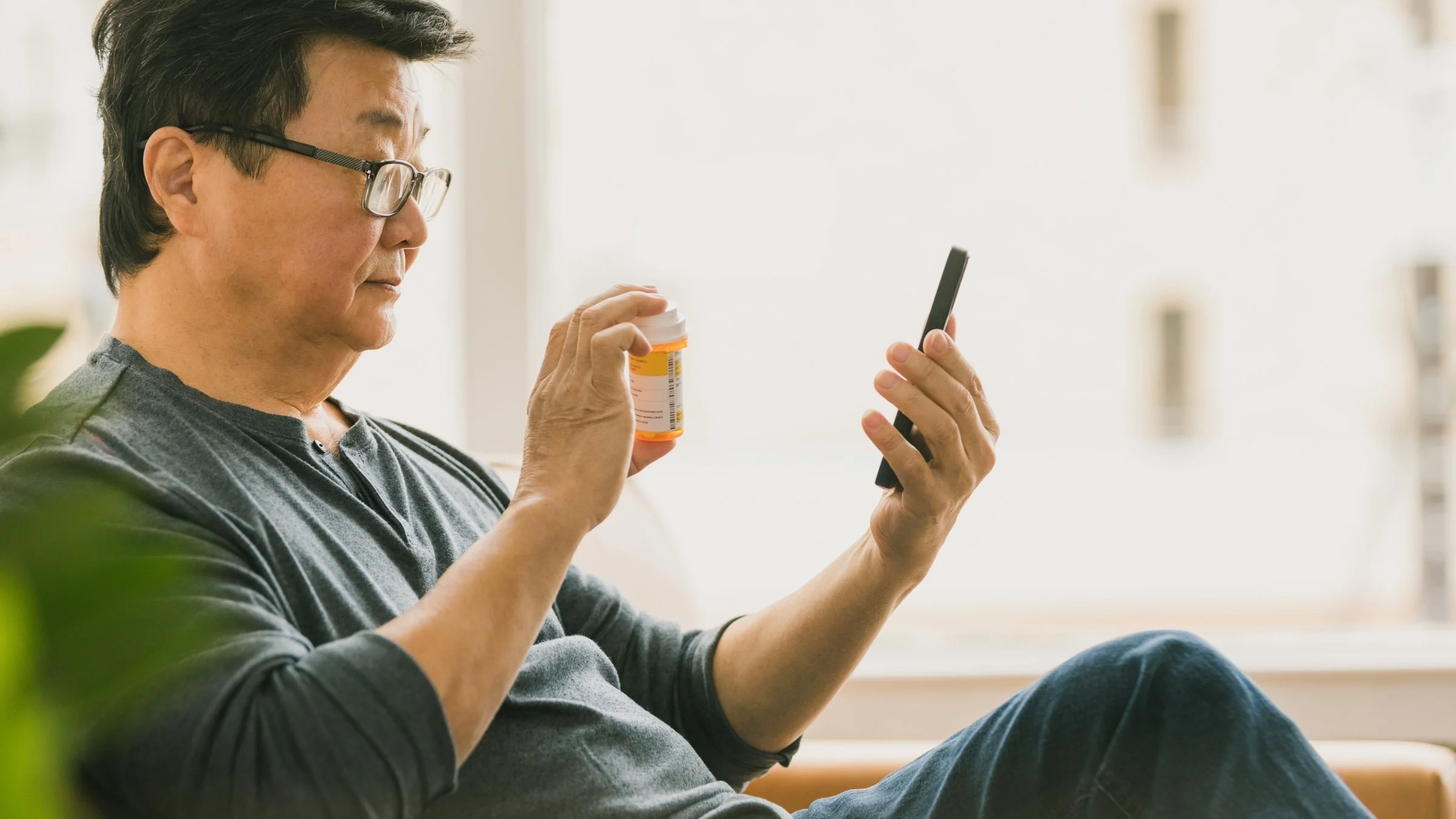 Older male showing off pill bottle to doctor on a telahealth visit on his cell phone.