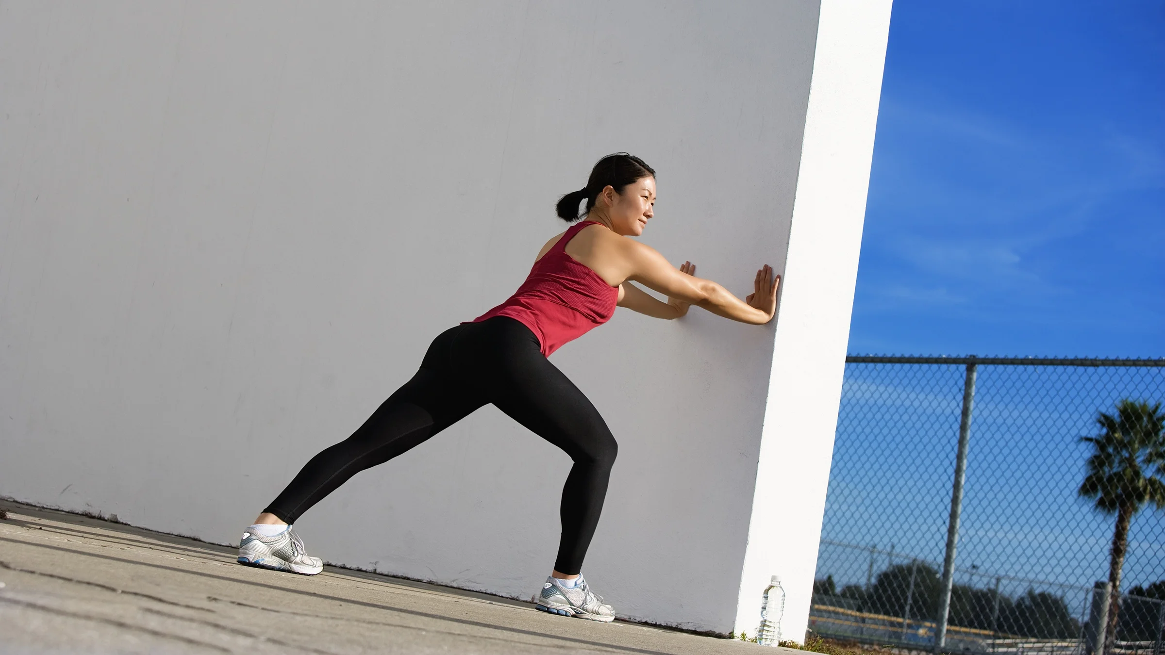 A woman is doing a calf stretch against a wall outdoors.