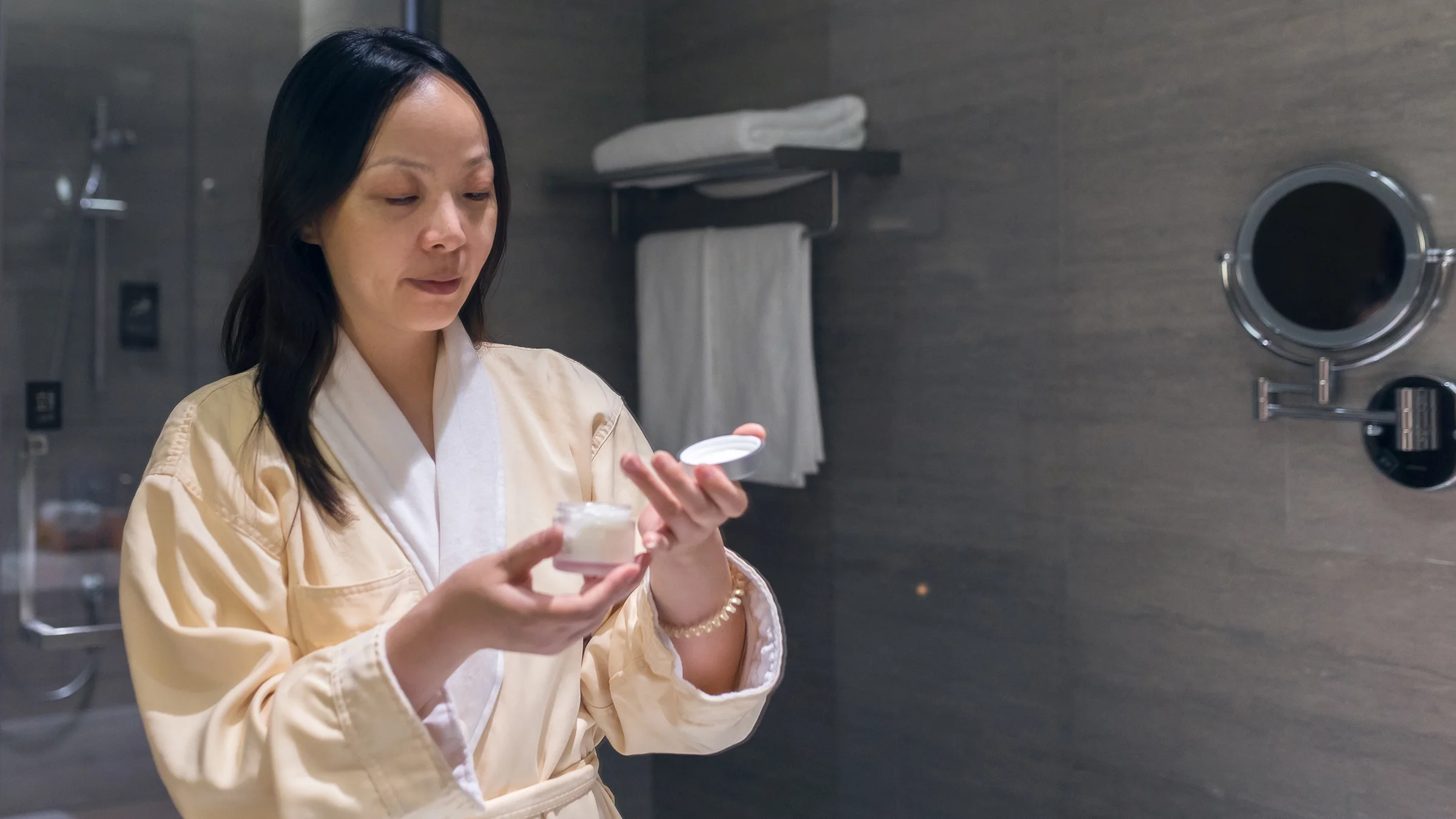 A woman opens a pot of facial cream. 