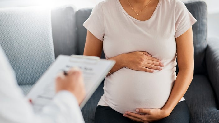 A pregnant woman is sitting on a couch at her doctor’s office in a close-up.