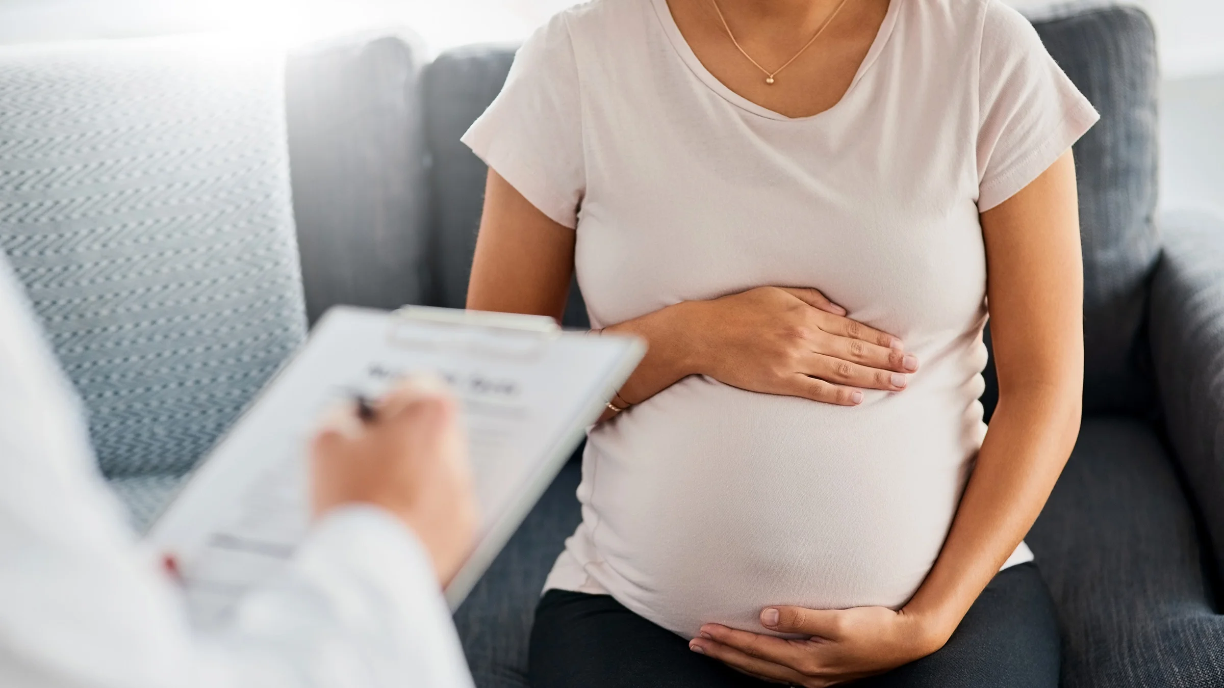 A pregnant woman is sitting on a couch at her doctor’s office in a close-up.