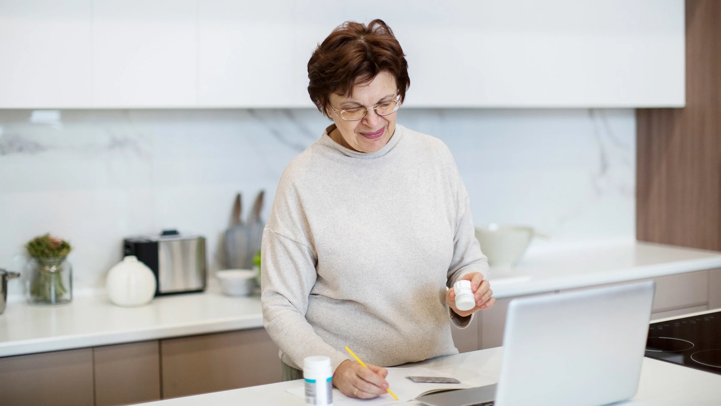 A person in a telehealth call holding pill bottles and taking notes.