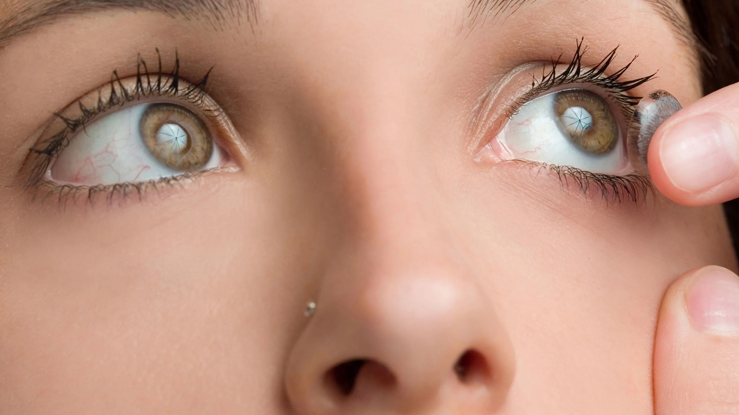 A woman puts a contact lens into her eye.