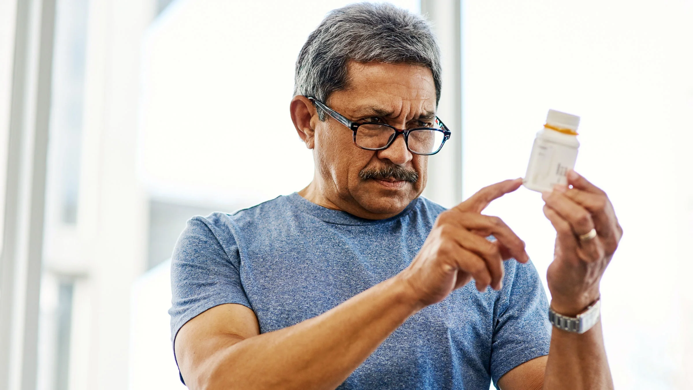 Man with glasses reads Rx bottle
