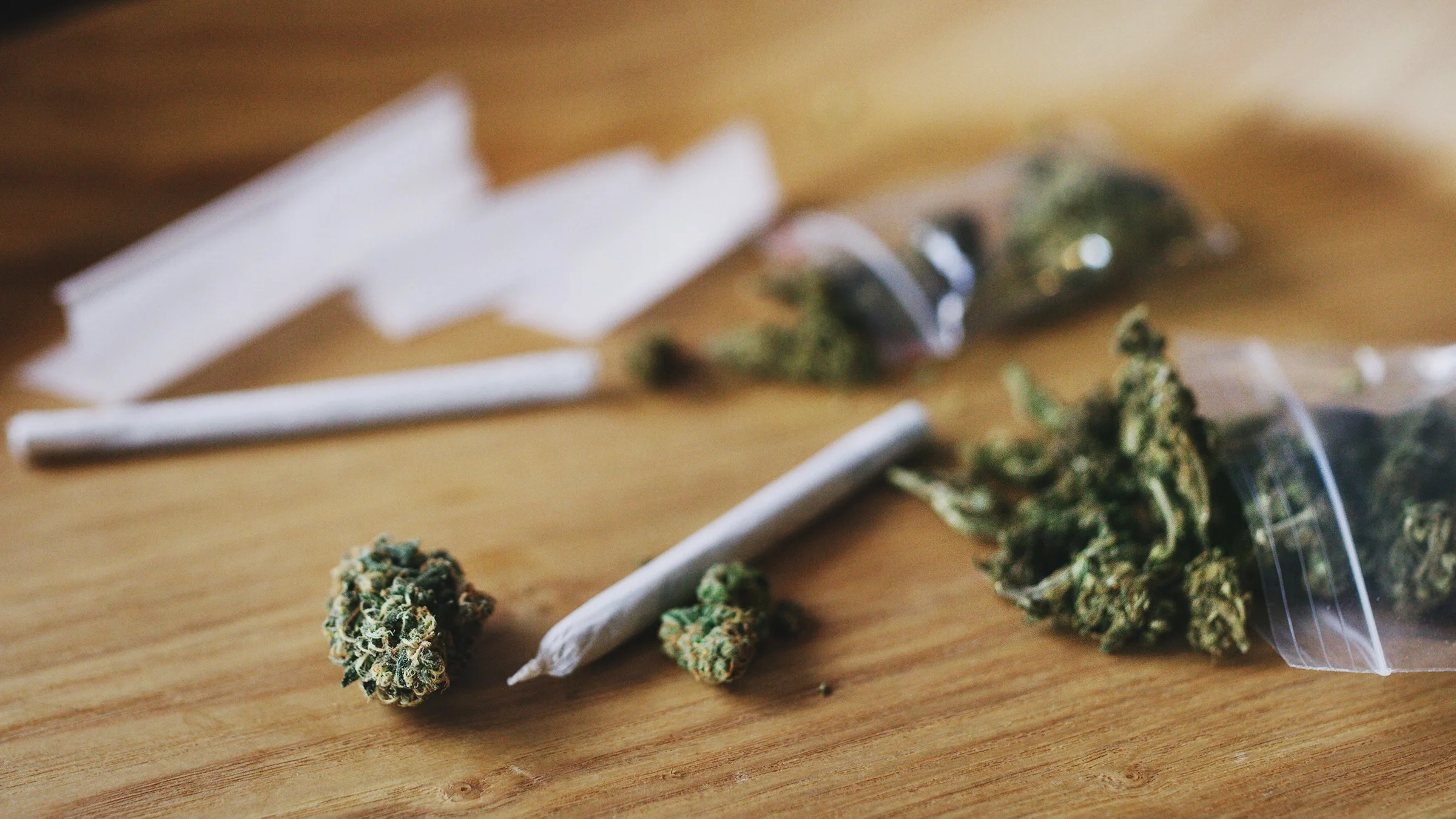 Marijuana bud and rolled joints on a wooden table.