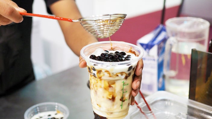 A person pouring brown sugar pearl boba over a glass of iced fresh milk.