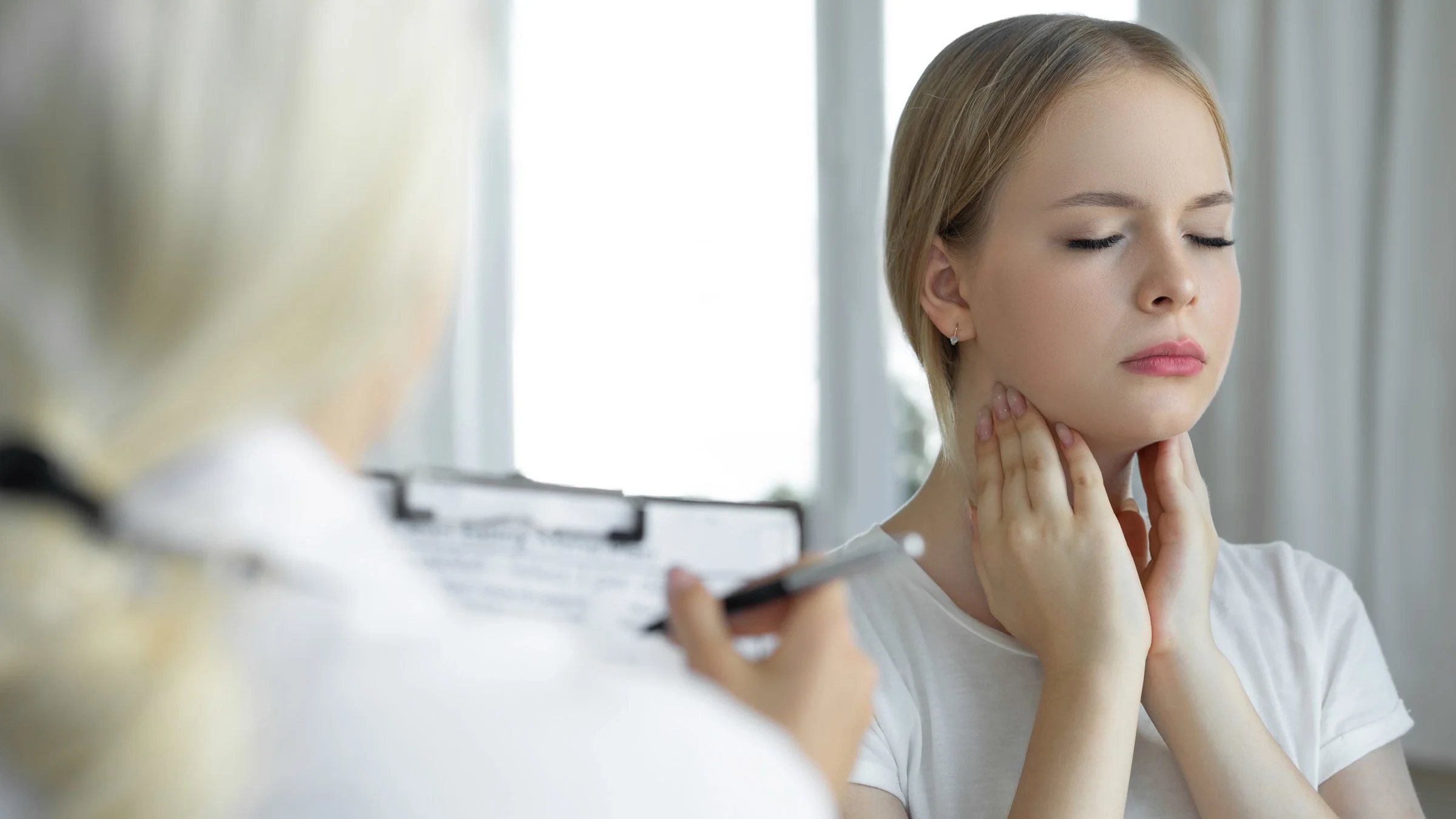 A patient touching their tonsils, while a doctor takes notes.