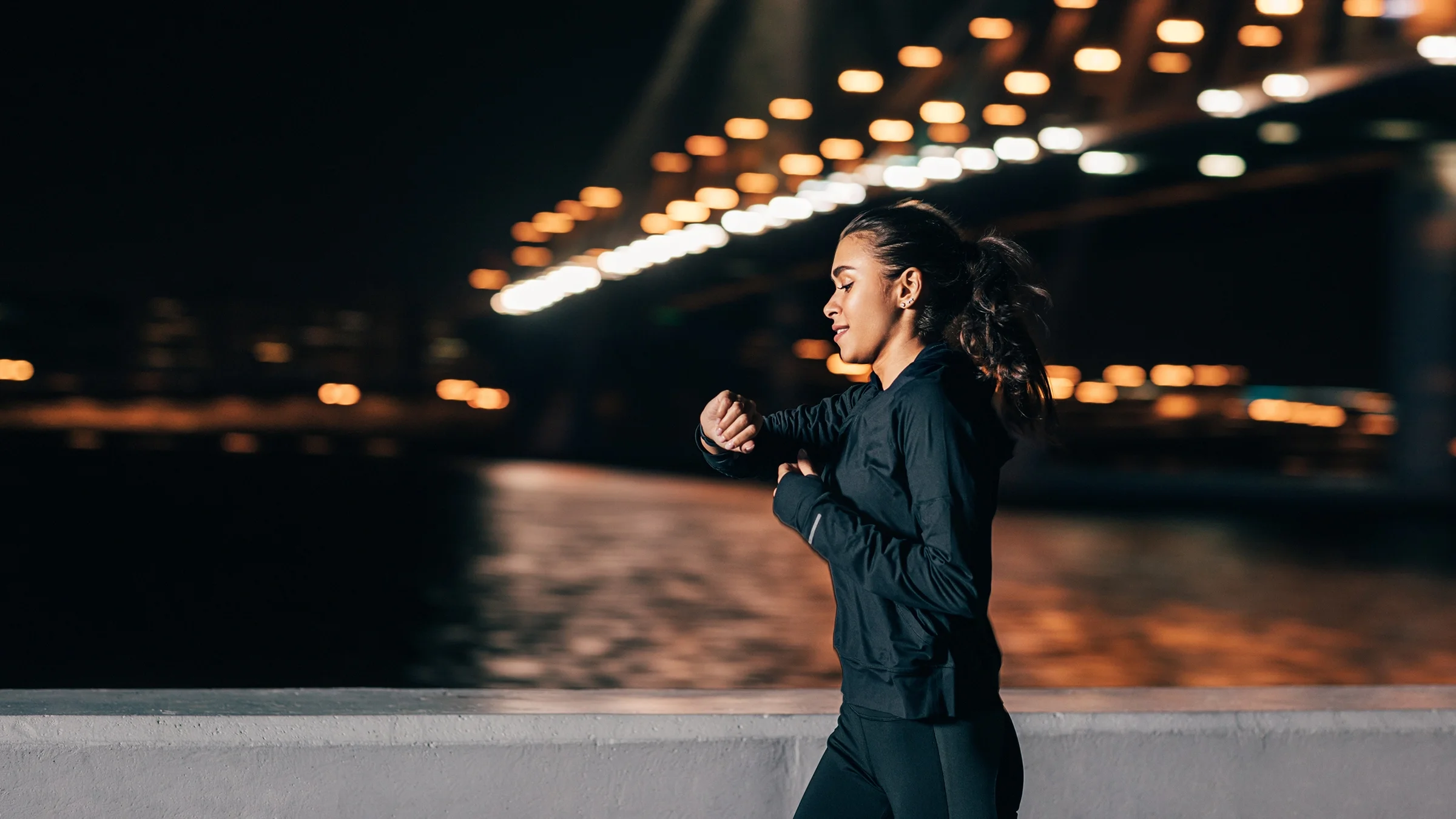 A woman is checking her watch while jogging at night.