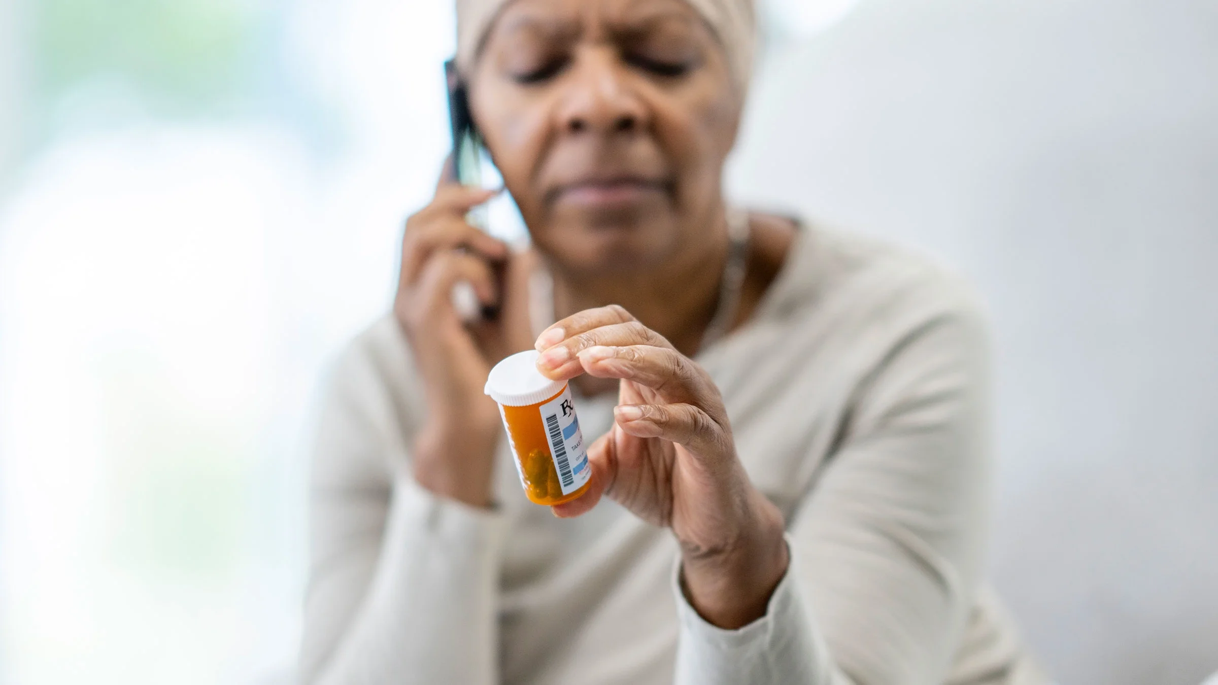 A woman calls in a prescription while holding a pill bottle.